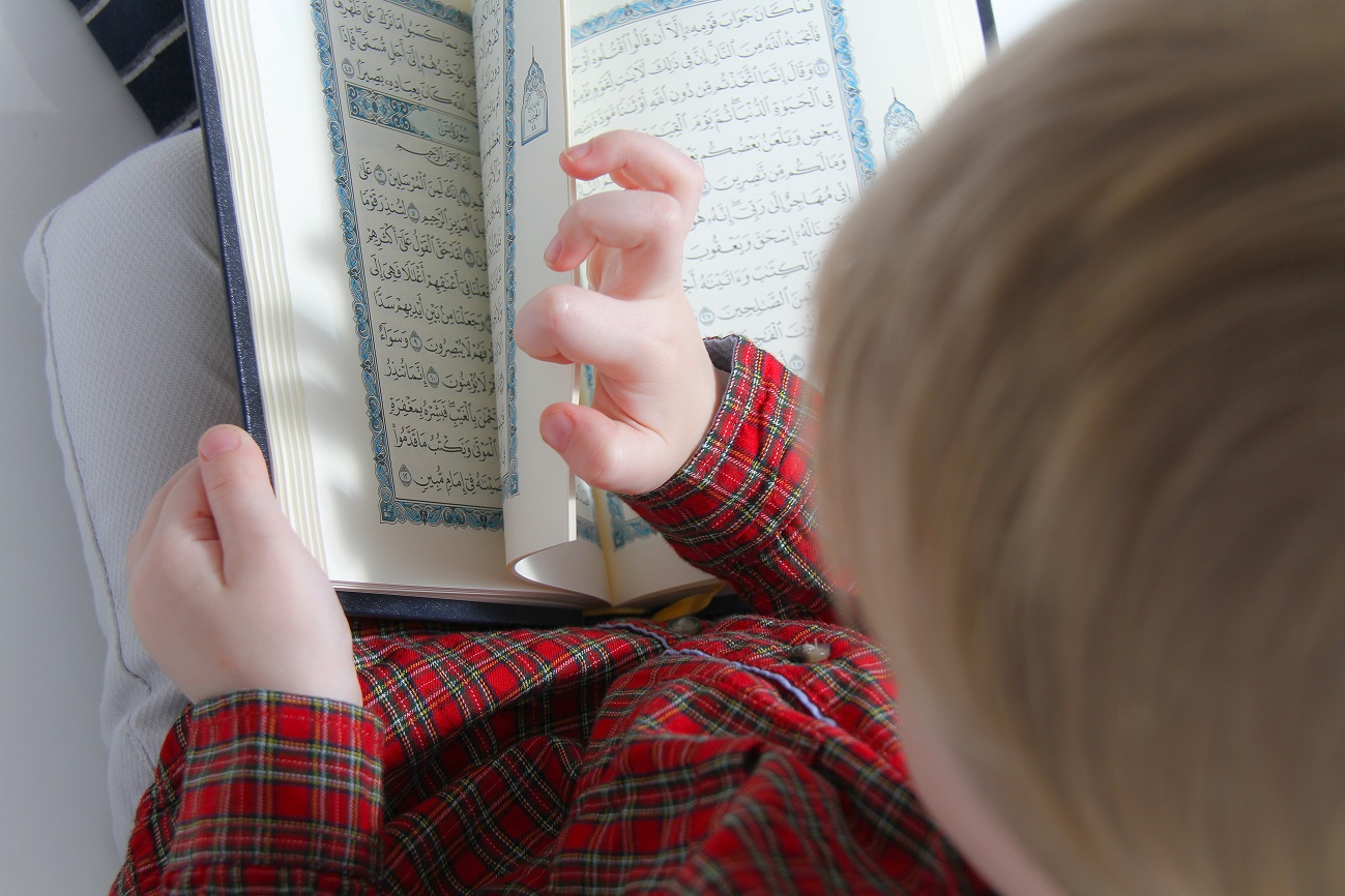 Little muslim European boy with islamic holy book Quran or Kuran